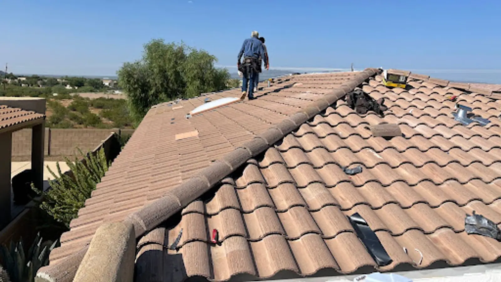 Two roofers walking the ridge of a concrete tile roof being re-laid, desert hills behind